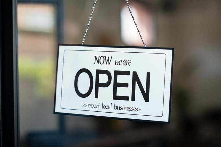 A business sign that says now we are open support local businesses on cafe or restaurant hang on door at entrance. Close up of open sign on the window of shop or store.