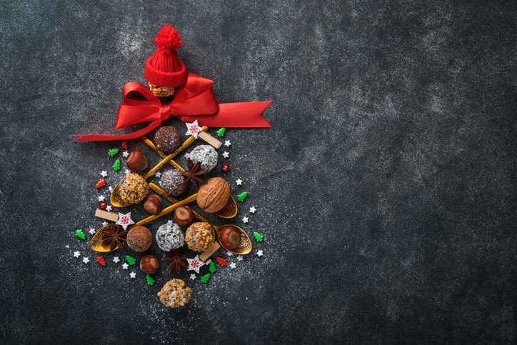 chocolate truffles and nuts forming a Christmas tree with sprinkles around them and a little knit red hat and bow on top