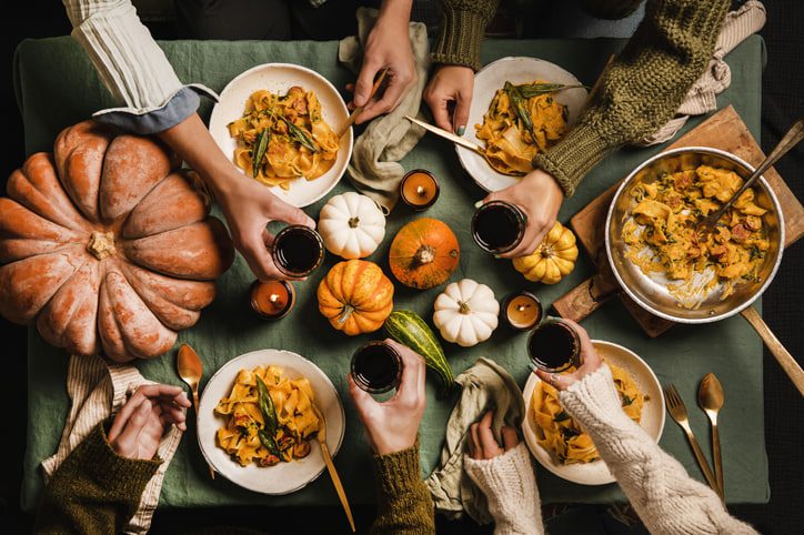 Fall table concept. Table with autumnal foods and pumpkin decor with arms reaching across to cheer during a meal time