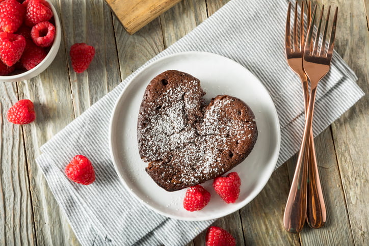 Heart shaped brownie with raspberries around it and two intertwined forks
